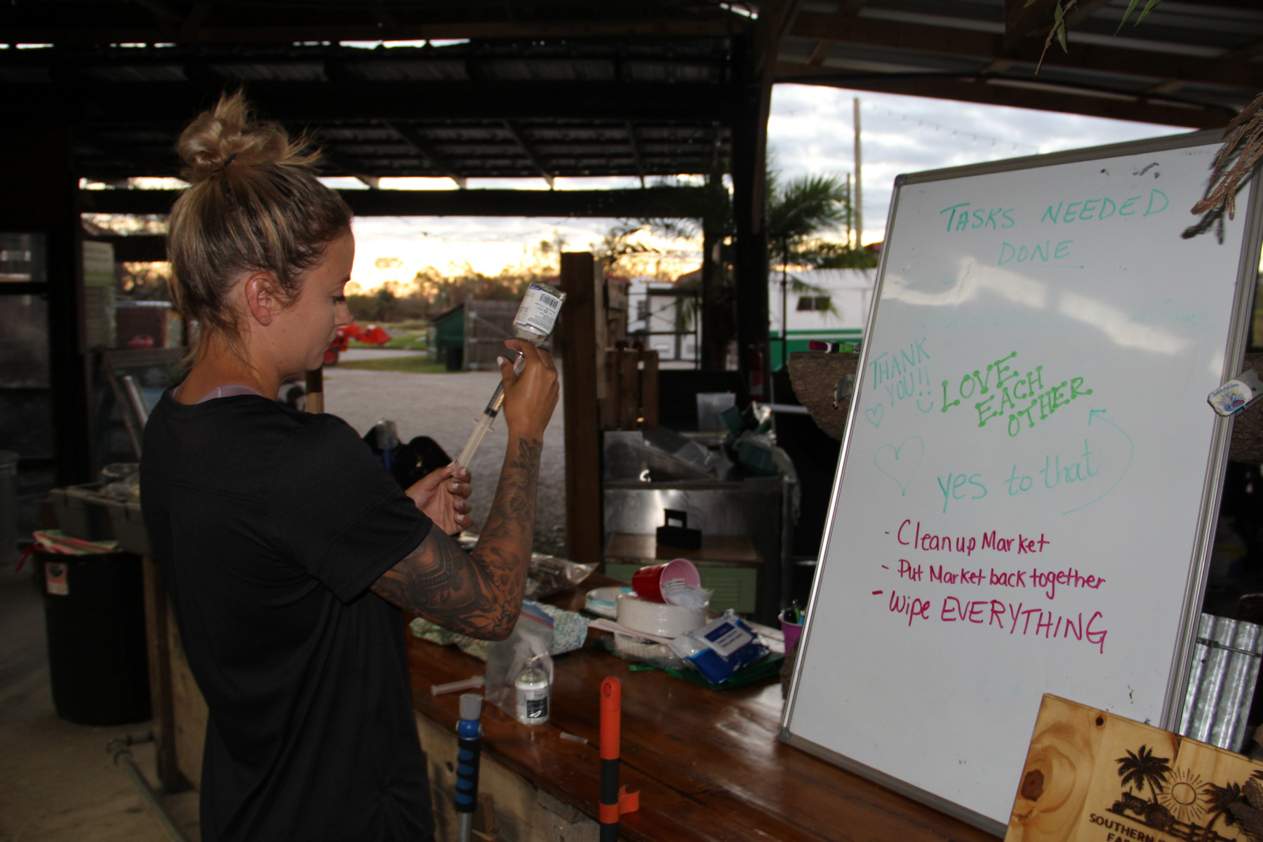 A woman holds a syringe up to a medicine vial next to a whiteboard with a checklist of things to do written on it.